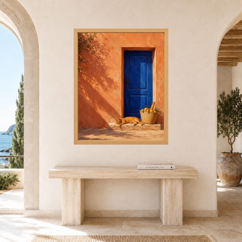 Pu&ograve; includere: Una stampa artistica incorniciata che raffigura una vivace parete in stucco arancione con una porta in legno blu intenso. Un gatto rosso riposa sulla soglia in pietra accanto a un cesto di vimini intrecciato pieno di limoni gialli e una baguette.