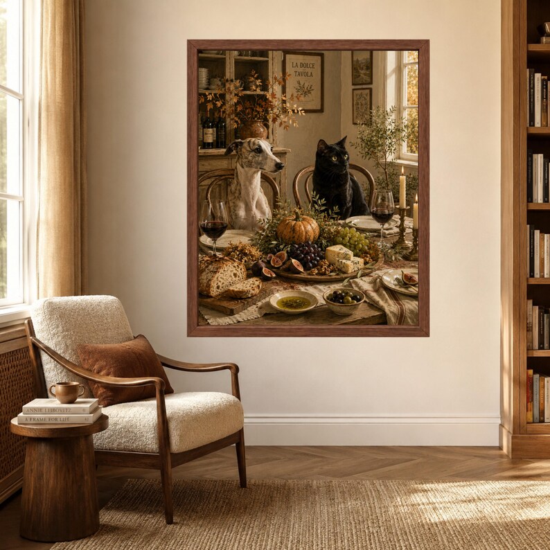 Op de afbeelding: Een ingelijste kunstdruk met een grijs-witte whippet en een zwarte kat aan een eettafel vol met een pompoen, druiven, vijgen, brood, olijven en wijnglazen. De sc&egrave;ne speelt zich af in een rustieke keuken met een houten buffetkast.