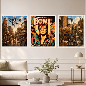 May include: Three framed wall art prints displayed in a row. The left print shows a bustling street scene titled Rhythm Row. The center print features a colorful portrait of David Bowie with the text Starman Rebel Icon. The right print depicts a person playing an acoustic guitar on a fire escape.