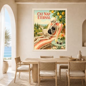 May include: A framed wall art print titled CAT NAP ETERNAL featuring a skeleton lounging on a red and white striped chair, reading a book with a black cat on its lap. A lemon tree, a small table with a drink, and sunglasses are visible.