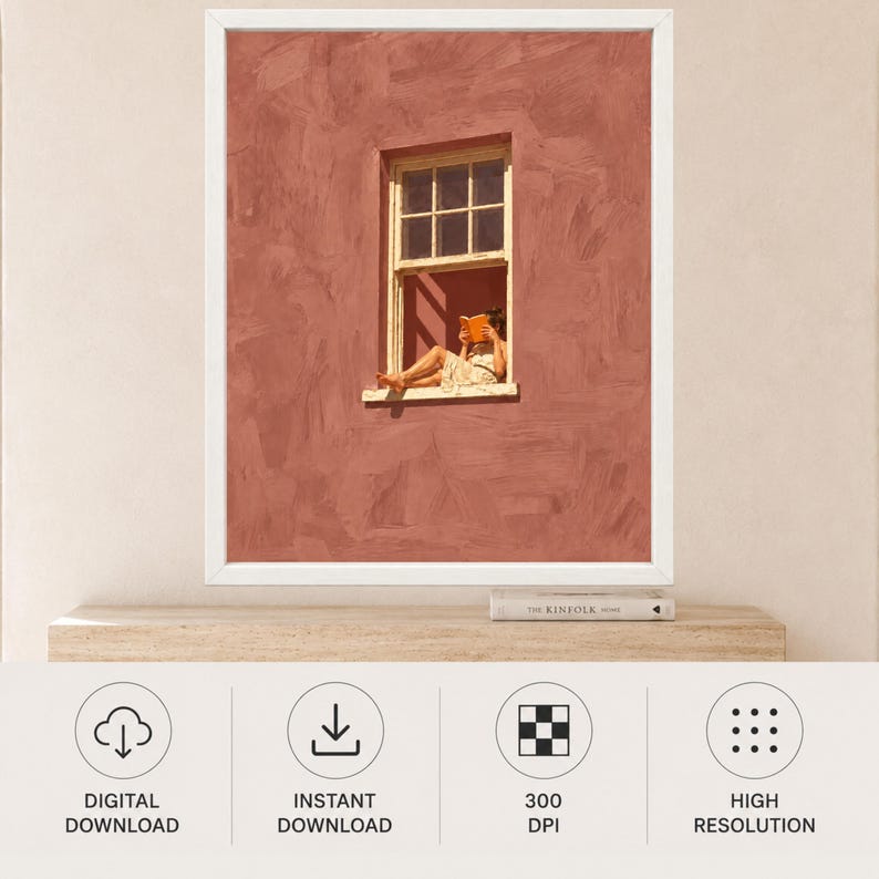 May include: A framed wall art print featuring a textured terracotta-colored wall with a white-framed window. A person sits in the window frame reading an orange book. The wall has visible brushstroke textures, and the window has a grid pane design.