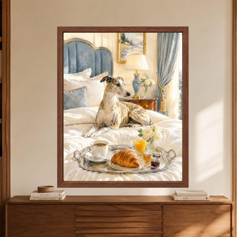 Framed greyhound wall art showing a brindle whippet resting on a white bed beside a silver breakfast tray with coffee, croissant, orange juice, preserves and flowers in a soft blue bedroom.