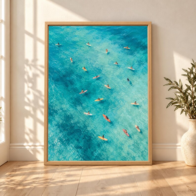 Framed aerial surf wall art showing multiple surfers on colorful surfboards scattered across bright turquoise, teal and aqua ocean water in a textured painterly coastal composition.