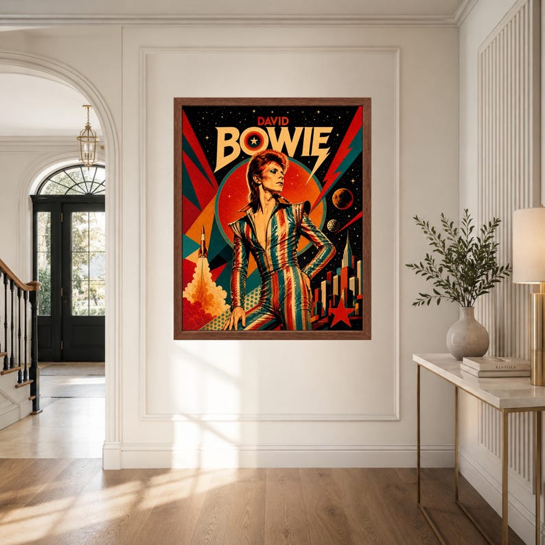 May include: A framed rectangular wall art print featuring a stylised illustration of David Bowie in a striped jumpsuit. The background displays a space theme with a rocket, planets, a large red sun, and a star, with the text DAVID BOWIE at the top.