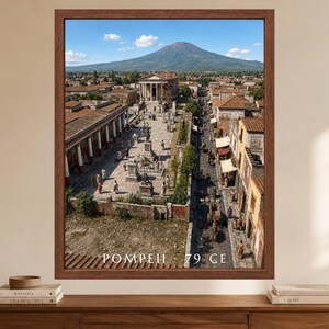 K&ouml;nnte beinhalten: Ein gerahmter Wandkunstdruck mit einer Luftaufnahme der antiken Stadt Pompeji vor dem Vesuv. Die Szene zeigt Steingeb&auml;ude, einen zentralen Platz mit Statuen und umhergehende Personen. Der Text lautet POMPEII 79 CE.
