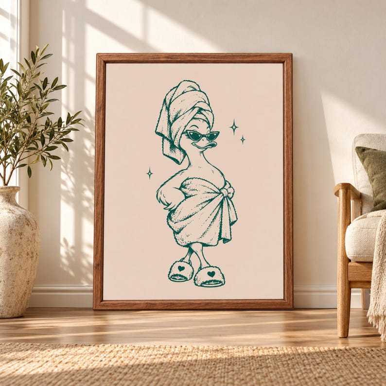Framed funny duck bathroom wall art featuring a duck in a towel turban, dark sunglasses, wrapped bath towel and fluffy heart slippers drawn in teal on a warm beige background.