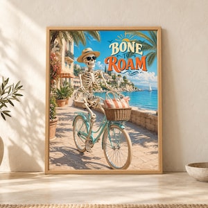 Framed Bone to Roam skeleton wall art showing a skeleton in sunglasses and a straw hat riding a turquoise bicycle beside a sunny Mediterranean coast with a wicker beach basket.