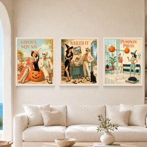 May include: Three framed wall art prints featuring vintage-style illustrations. The first shows a person and a skeleton with a pumpkin and black cat labeled GHOUL SQUAD. The second shows a person and skeleton labeled NAILED IT. The third shows a skeleton lifting pumpkins labeled PUMPKIN PRESS.