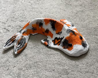 Op de afbeelding: Een handbeschilderd koi-visbeeldje met een textuurrijke witte basis en levendige oranje en zwarte vlekken. De vis heeft twee kleine zwarte kraaltjes als ogen en een klein zwart hartvormig detail op de zijkant bij de borstvin.
