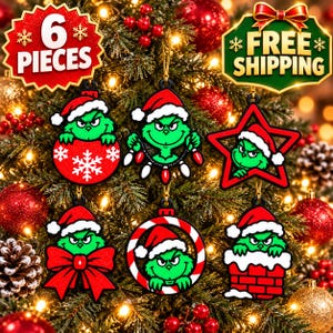 Puede incluir: Un conjunto de seis adornos planos para árbol de Navidad con un personaje verde que lleva un gorro de Papá Noel rojo. Los diseños incluyen al personaje en una bola roja con copos de nieve, sosteniendo luces, dentro de una estrella roja, con un lazo rojo, en un anillo de bastón de caramelo y en una chimenea de ladrillo.