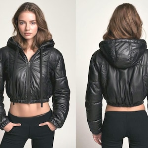 May include: A black cropped puffer jacket featuring a hood with black drawstrings, a front zip fastening, and long sleeves with elasticated cuffs. The jacket has a quilted texture and a hem that sits above the waistline, shown from front and back.