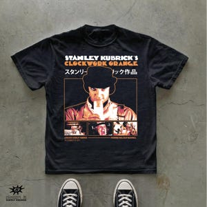 May include: A black short-sleeve t-shirt featuring a graphic print of the film A Clockwork Orange. The design includes the title in English and Japanese, a central portrait of the main character, and three smaller film stills at the bottom.