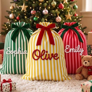 Pode incluir: Três sacos de presente de tecido com listras verticais em verde, amarelo e vermelho. Cada saco apresenta um laço de veludo no topo e um nome em letra cursiva: Sophia em branco, Olive em vermelho e Emily em branco. Um urso de pelúcia.