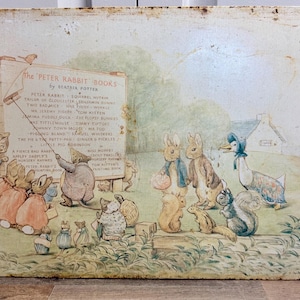 May include: A rectangular metal sign featuring a vintage illustration of Beatrix Potter characters gathered around a signpost titled The Peter Rabbit Books. The artwork displays various animals in soft, muted colors with visible rust along the edges.