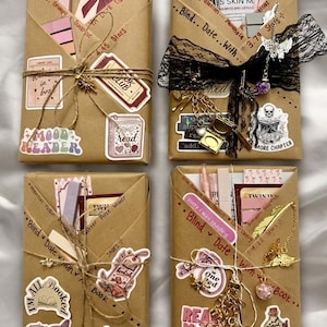 May include: Four rectangular packages wrapped in brown paper, each tied with twine and decorated with various stickers, charms, and handwritten text. The packages feature assorted items like bookmarks, pens, and small trinkets, creating a curated gift set for readers.