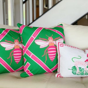 May include: Three decorative throw pillows with a green and pink geometric pattern featuring a stylized bee design. One pillow has a white background with a pink and green stylized monkey design.