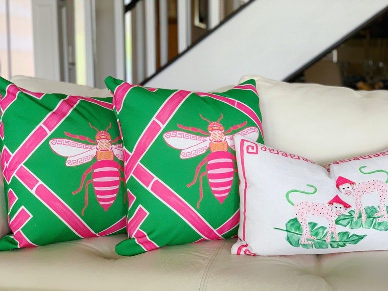 May include: Three decorative throw pillows with a green and pink geometric pattern featuring a stylized bee design. One pillow has a white background with a pink and green stylized monkey design.