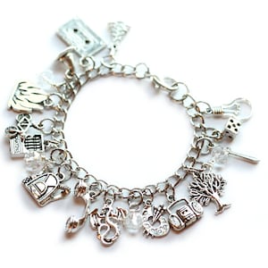 Puede incluir: Pulsera de plata con dijes variados, incluyendo una cinta de cassette, un árbol, un dragón, un teléfono y un radiocasete. La pulsera tiene un cierre de mosquetón y está adornada con pequeñas cuentas transparentes.