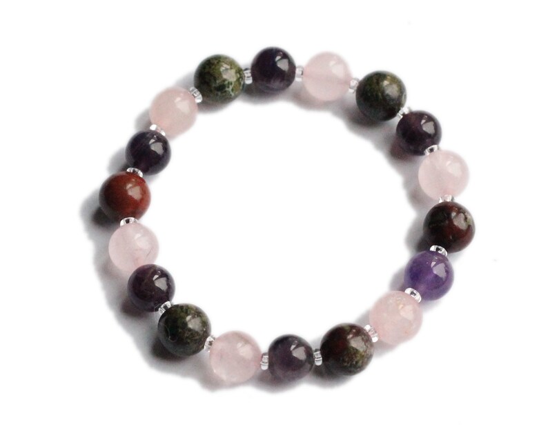 May include: A bracelet made with round, multi-colored gemstone beads. The beads are pink, red, purple, and green.