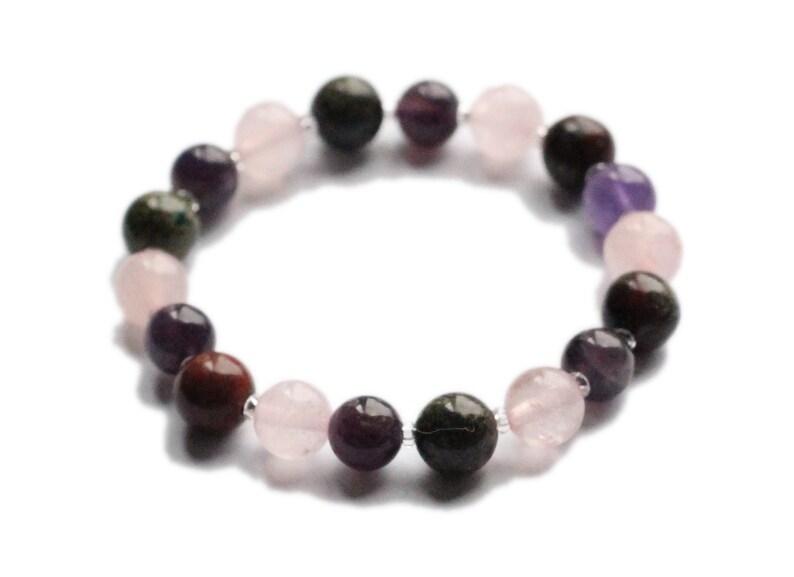 May include: A bracelet made of various gemstone beads, including pink, purple, and green. The beads are strung on a clear elastic cord.