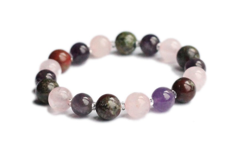 May include: A bracelet made of various colored gemstone beads, including pink, purple, red, and green. The beads are strung on a silver cord.