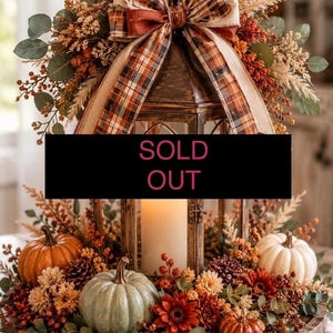 May include: A decorative lantern centrepiece featuring a plaid ribbon bow, surrounded by artificial pumpkins, pinecones, and autumn-coloured flowers. A black rectangular sign with the text SOLD OUT is placed across the centre of the lantern.