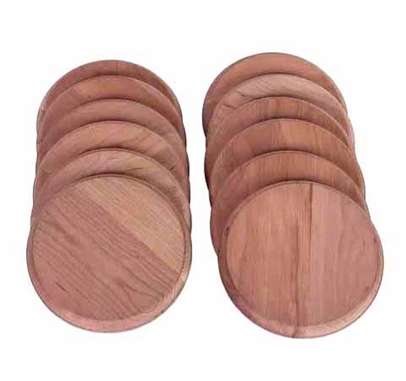 May include: Two stacks of round, wooden coasters. Each coaster is a light brown color with visible wood grain. The coasters are arranged in a fan-like pattern, showcasing their circular shape and natural wood texture.