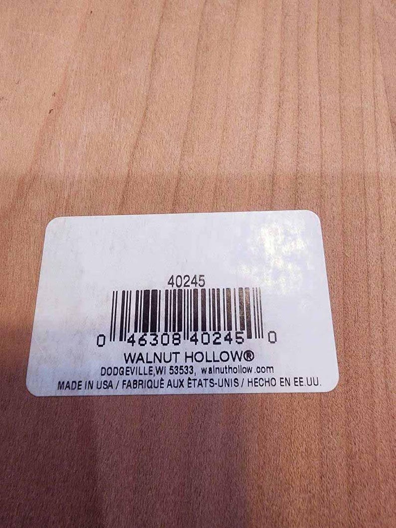 May include: A white rectangular label with a barcode and the text "WALNUT HOLLOW&reg;" printed in black. The label also includes the text "MADE IN USA / FABRIQUE AUX &Eacute;TATS-UNIS / HECHO EN EE.UU." on a light brown wooden surface.