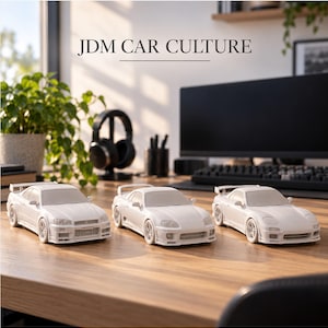 May include: Three white scale model sports cars arranged on a wooden desk. The cars feature detailed body kits, rear spoilers, and low-profile wheels. The text JDM CAR CULTURE is displayed in the upper center of the frame above the car models.