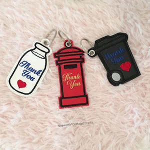 May include: Three keychains with the words "Thank You" embroidered on them. The keychains are shaped like a milk bottle, a red post box, and a black bin. Each keychain has a small red heart embroidered on it.