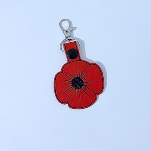 May include: Red leather poppy keyring with a black centre and a silver metal ring.