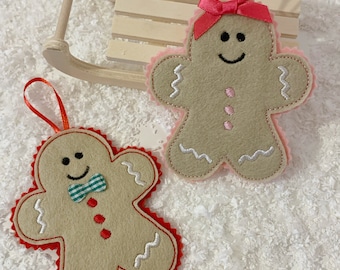 May include: Two felt gingerbread people ornaments, one with a pink bow and the other with a green bow tie. Both have white stitching and are decorated with red and pink dots.