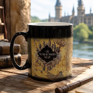 May include: A black ceramic mug featuring a tan-colored parchment graphic with the text The Marauder's Map and an illustration of a castle. The mug has a curved handle and a white interior, displaying detailed cartographic lines and markings.