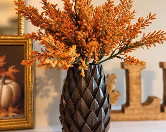 May include: A dark brown vase with a textured, overlapping leaf-like pattern holds a large arrangement of vibrant orange, feathery stems. The vase has a rounded, tapered shape and a matte finish, contrasting with the bright, textured orange foliage.