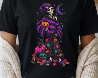 Könnte beinhalten: Ein schwarzes T-Shirt mit einer Grafik eines Skeletts, das einen lila-schwarz gestreiften Pullover, eine passende Mütze und eine mit bunten Kürbissen verzierte Hose trägt. Der Text Spooky Season steht bei einem rosa Kürbis.