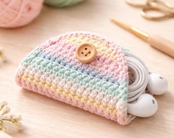 Könnte beinhalten: Ein halbkreisförmiges Häkeltäschchen mit pastellfarbenen Regenbogenstreifen in Rosa, Gelb und Blau. Das Täschchen wird mit einem hellbraunen Holzknopf verschlossen und enthält ein Paar weiße kabelgebundene Ohrhörer im Inneren.