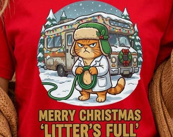 Könnte beinhalten: Ein rotes T-Shirt mit einer Grafik einer orangefarbenen Katze, die eine grüne Trappermütze und einen weißen Mantel trägt und einen grünen Schlauch vor einem Wohnmobil im Schnee hält. Der Text darunter lautet MERRY CHRISTMAS LITTER'S FULL in Gelb.