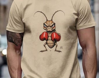Könnte beinhalten: Ein beiges T-Shirt mit kurzen Ärmeln und einer grafischen Illustration eines braunen Insekts, das aufrecht steht und rote Boxhandschuhe trägt. Das Insekt hat einen grimmigen Gesichtsausdruck, lange Fühler und eine Signatur.