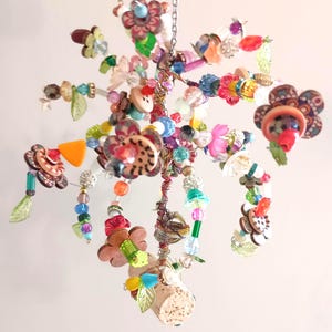 May include: A hanging mobile ornament constructed from a central cork base with radiating wire branches. The structure is adorned with a variety of colorful beads, buttons, and translucent leaf-shaped charms in shades of pink, blue, green, and orange.