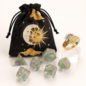 May include: A black drawstring pouch featuring a gold sun and moon illustration with the text I LOVE YOU LIKE THE MOON LOVES THE SUN, six translucent polyhedral dice with iridescent flakes and gold numbers, and a gold ring with sun and moon motifs.