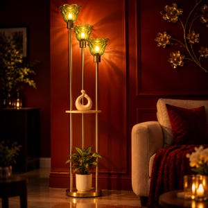 May include: A tall gold floor lamp featuring three vertical poles of varying heights, each topped with a green glass flower-shaped shade. A circular wooden shelf holds a white ceramic abstract sculpture and a potted green plant.