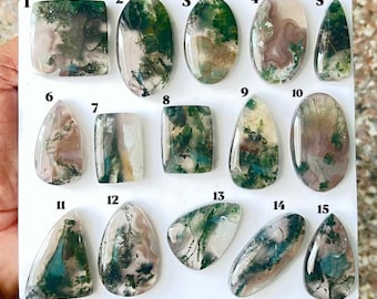 Puede incluir: Una colección de quince cabujones de ágata musgosa pulidos dispuestos en un tablero blanco, numerados del uno al quince. Cada gema presenta bases translúcidas blancas, grises y claras con distintas inclusiones verdes tipo musgo.
