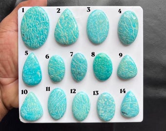 Puede incluir: Una colección de catorce piedras preciosas pulidas de color turquesa dispuestas en una tarjeta de presentación rectangular blanca. Cada piedra está numerada del 1 al 14 y presenta patrones de vetas blancas únicos en formas ovaladas, de lágrima y redondeadas.