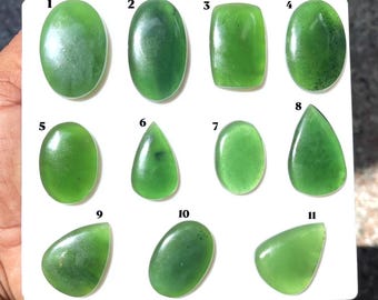 Puede incluir: Once cabujones de jade verde pulidos dispuestos en una tarjeta de presentación blanca, numerados del uno al once. Las piedras presentan varias formas, incluyendo ovaladas, rectangulares, de pera y de lágrima, con superficies lisas y tonos verdes.
