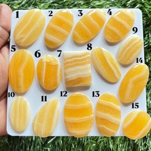 Pode incluir: Uma cole&ccedil;&atilde;o de quinze caboch&otilde;es de &aacute;gata com faixas amarelas e brancas dispostos num cart&atilde;o de apresenta&ccedil;&atilde;o branco. As pedras est&atilde;o numeradas de 1 a 15 e apresentam v&aacute;rias formas ovais, retangulares e de gota com superf&iacute;cies lisas.