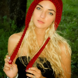 Puede incluir: Una mujer con el pelo largo y rubio lleva un gorro de punto rojo con la parte superior puntiaguda. El gorro tiene lazos largos que le cuelgan por la espalda. Lleva un top negro sin tirantes.