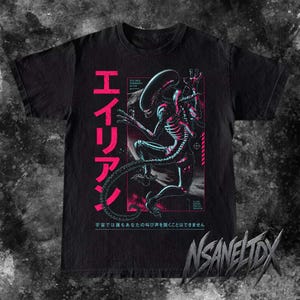 Peut inclure: Un t-shirt noir avec un graphique représentant une créature xénomorphe dans des tons de bleu et de rose. Le design comprend de grands caractères japonais en rose, du texte technique plus petit et la phrase 宇宙では誰もあなたの叫び声を聞くことはできません.