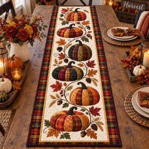 May include: A rectangular table runner featuring a cream-colored center panel with a quilted pattern of six pumpkins in various plaid and floral fabrics, surrounded by autumn leaves, acorns, and pinecones, framed by a dark plaid border.
