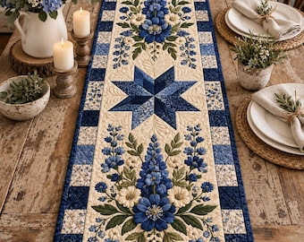 May include: A rectangular quilted table runner featuring a central dark blue star pattern flanked by two symmetrical floral arrangements of blue delphiniums and white flowers on a cream background, bordered by a blue and white checkered fabric trim.