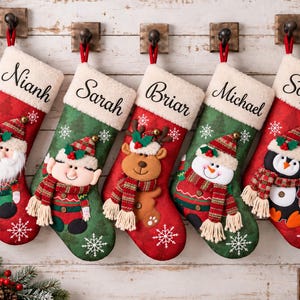 Op de afbeelding: Vijf kerstsokken in rood en groen met witte randen van imitatiebont, gepersonaliseerd met de namen Nianh, Sarah, Briar, Michael en Sophia. De sokken zijn voorzien van applicaties van de kerstman, een elf, rendier, sneeuwpop en pinguïn.